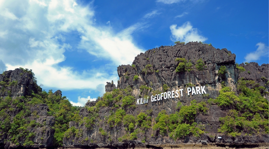 A scenic shot of the Kilim Geoforest Park's cliffside sign, with a blue sky.