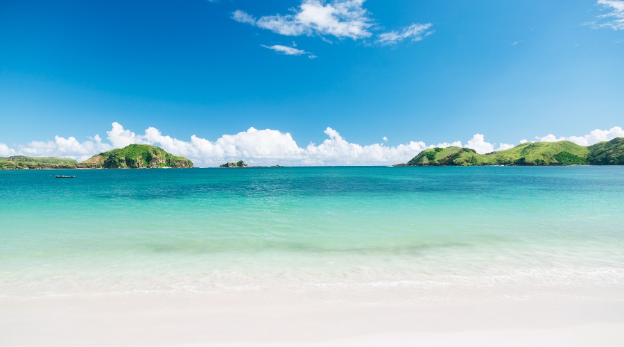 Tranquil Pantai Kok beach in Langkawi with clear waters, soft sand, and limestone hills in the distance.